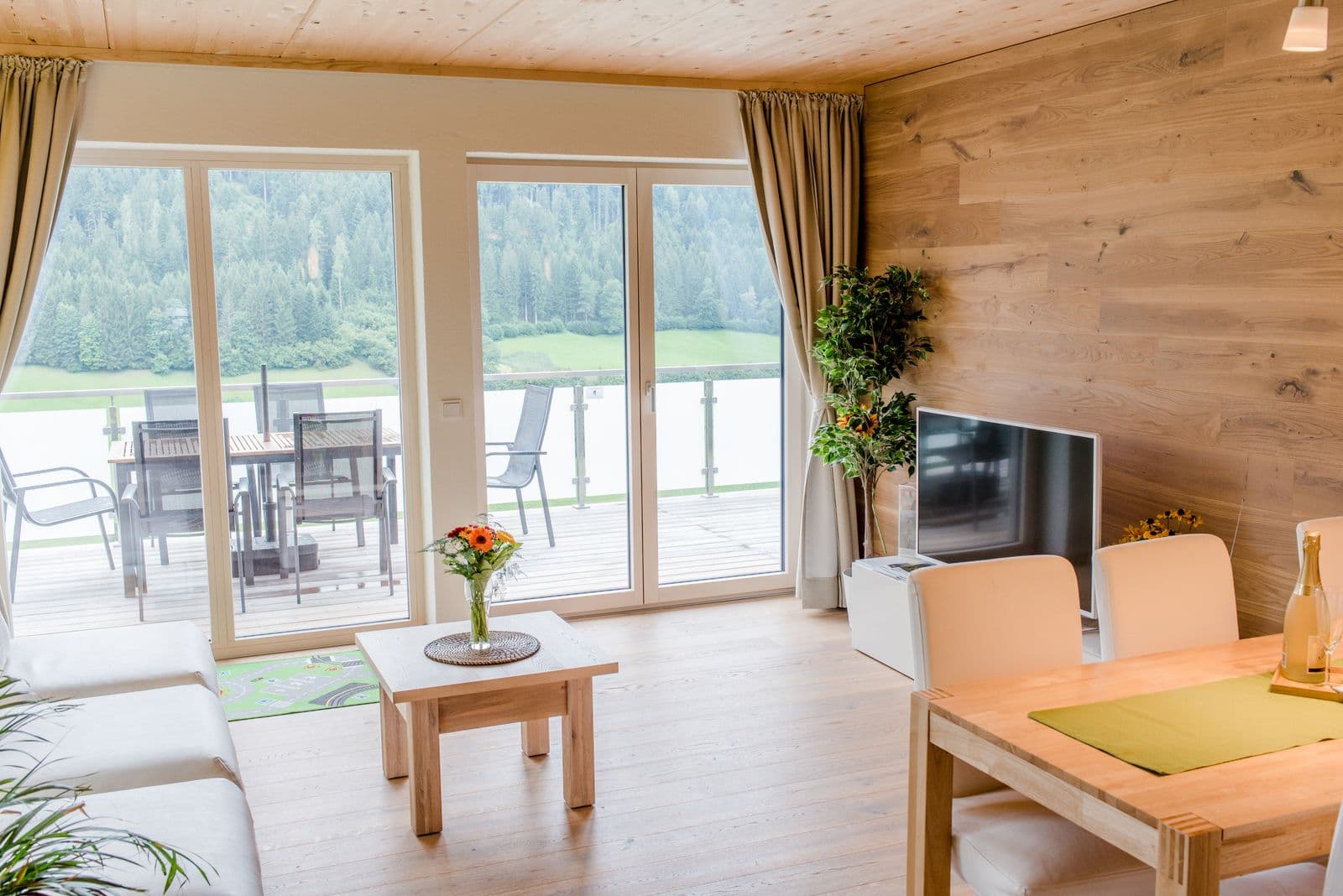 Heller Wohnraum mit Sofa, Tisch und großen Fenstern ins Grüne.
